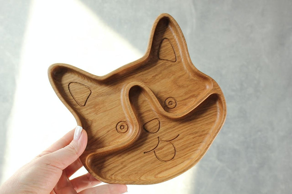 5. Person holding corgi-shaped wooden plate for kids, showing two sectors and engraved details, against a grey background.