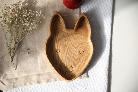 4. Front view of wooden fox-shaped plate on beige cloth with red apple and white flowers, highlighting engraved face details