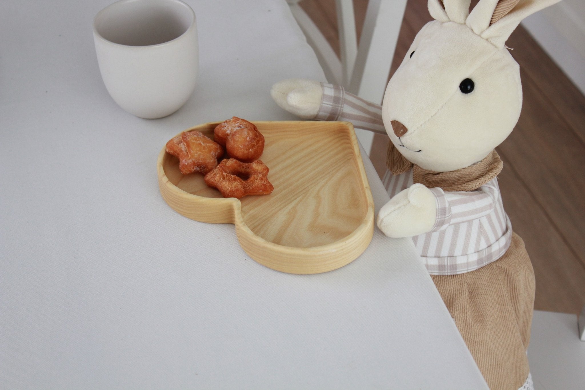 4. Plush toy rabbit at table with heart-shaped wooden plate containing snacks, next to white mug