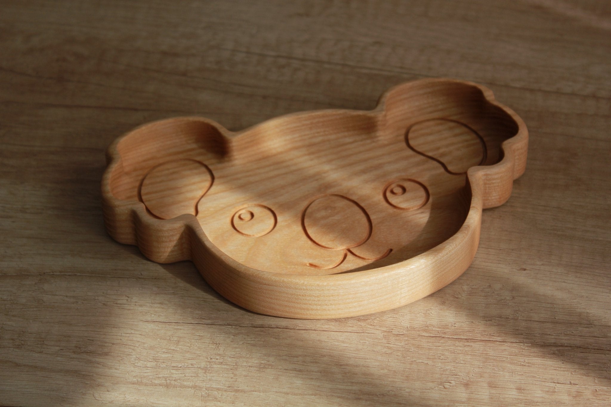 2. Studio shot of wooden koala-shaped plate on wooden surface, highlighting smooth ash wood texture and engraved facial features