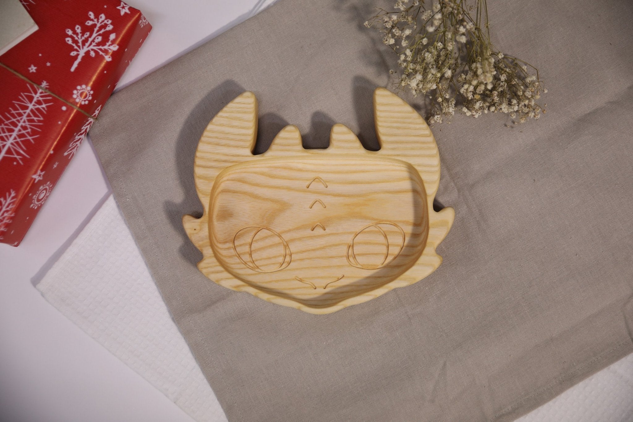 6. Handmade wooden kids plate shaped like a character face, made from light oak or ash wood, placed on a beige cloth with decorative flowers