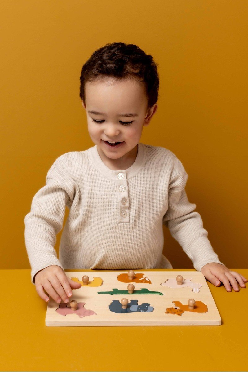 1. Child playing with Trixie Baby Animals wooden puzzle featuring colorful animal pieces on a yellow background