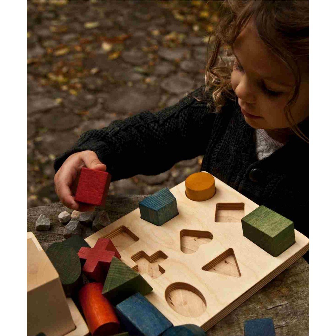 1. Child playing with Wooden Story shape sorting blocks on outdoor table, featuring colorful wooden shapes and board