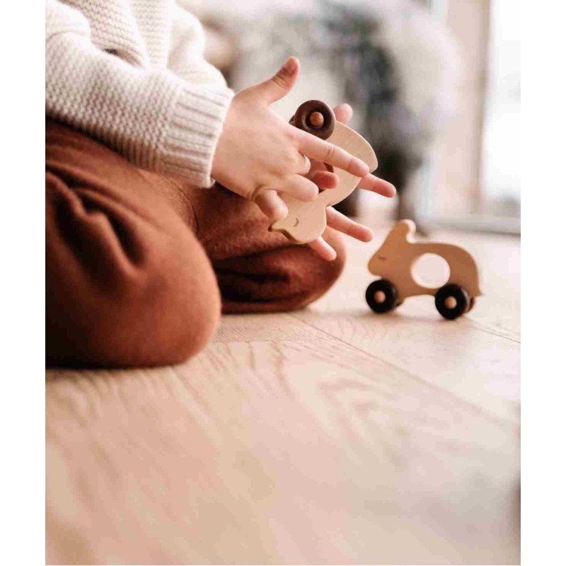 1. Child sitting on wooden floor holding Wooden Story duck toy with another toy nearby