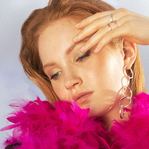 1. Woman wearing large silver hoop earrings with pink feather boa, showcasing MyaMoon jewelry in a vibrant setting